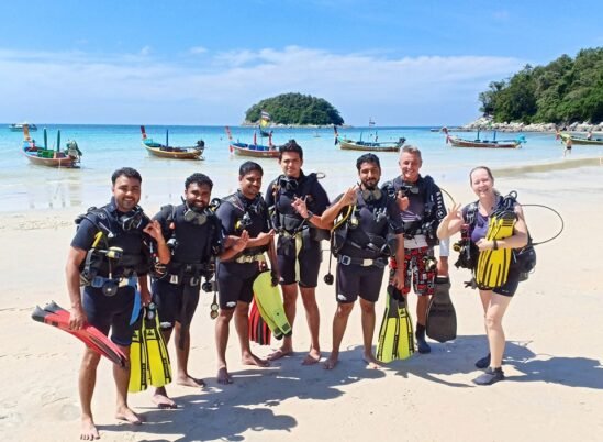A group of students with their instructors are on the sand at Kata Beach preparing to walk into the water for their dive.